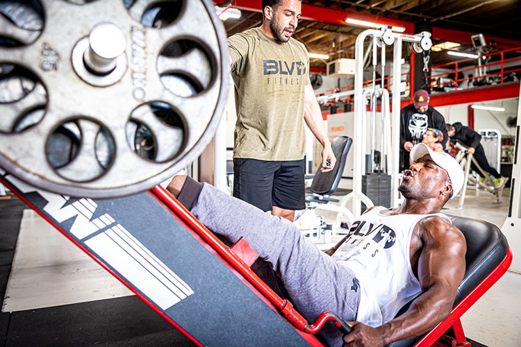 A trainer spotting a member on a leg press at Boulevard Fitness